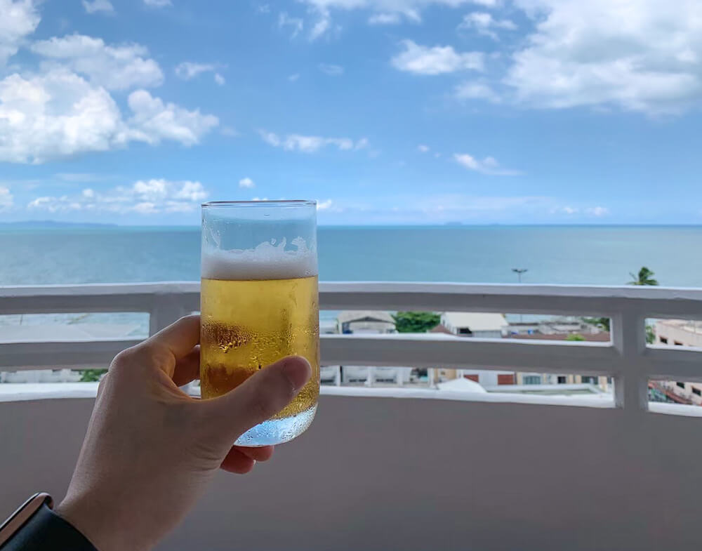ディー ワーリー ジョムティエン ビーチ パタヤ ホテル（D Varee Jomtien Beach Pattaya Hotel）の客室バルコニーで海を見ながらビールを飲む